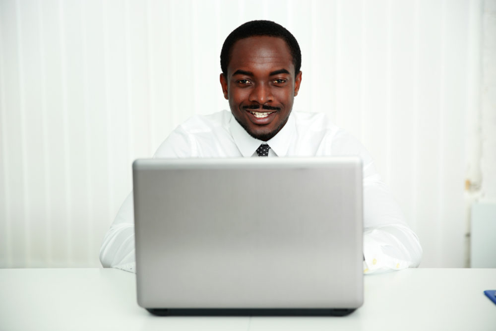 Portrait Of A Smiling African Businessman Sitting At The Table With Laptop In Office